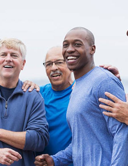 Multi-ethnic group of men standing together, smiling, supporting one another. Mixed ages ranging from 20s to 70s.